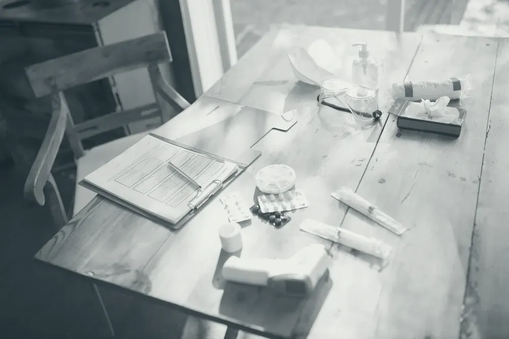 A wooden table with a thermometer, a face mask, tablets and home care items arranged in natural light.