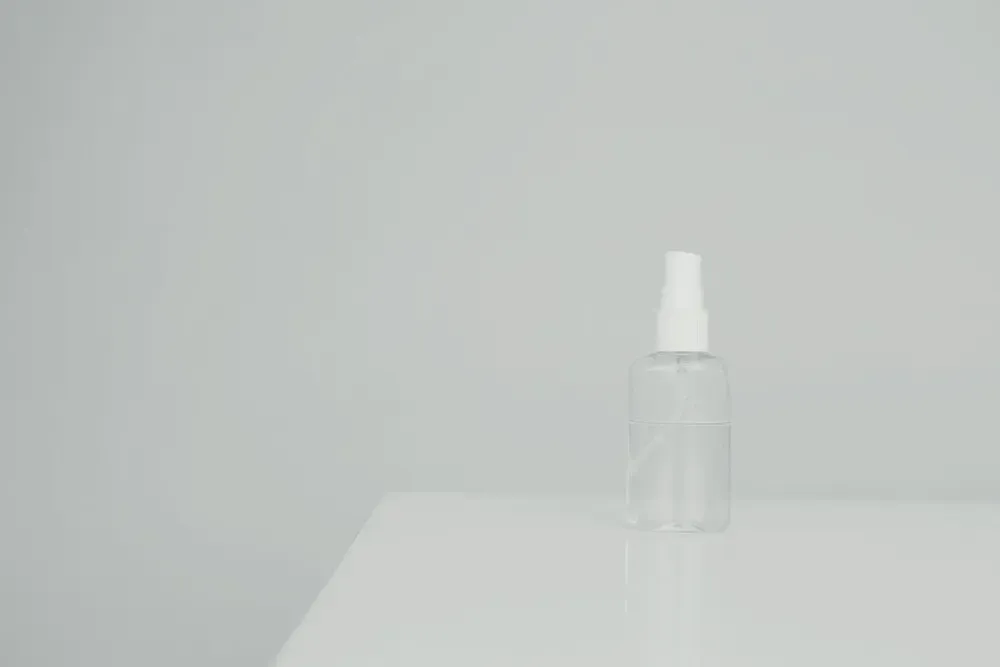 A clear spray bottle on a white table, with a beige wall behind it.