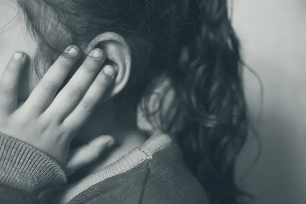 Close-up of a hand pressed against an ear, the common gesture of someone with ear pain.