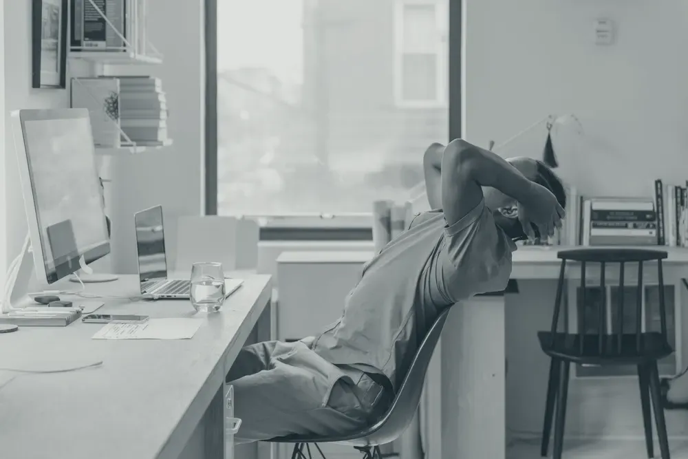 A man leaning back in an office chair, arching his back with his arms behind his head.