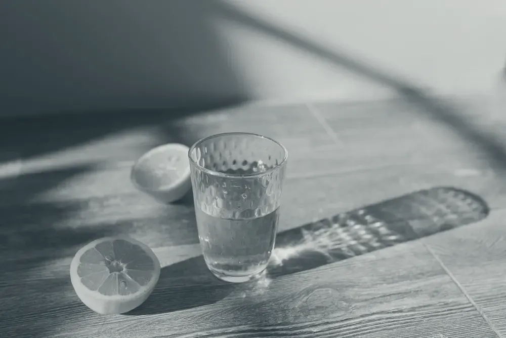 A glass of water with lemon slices on a sunlit wooden table.