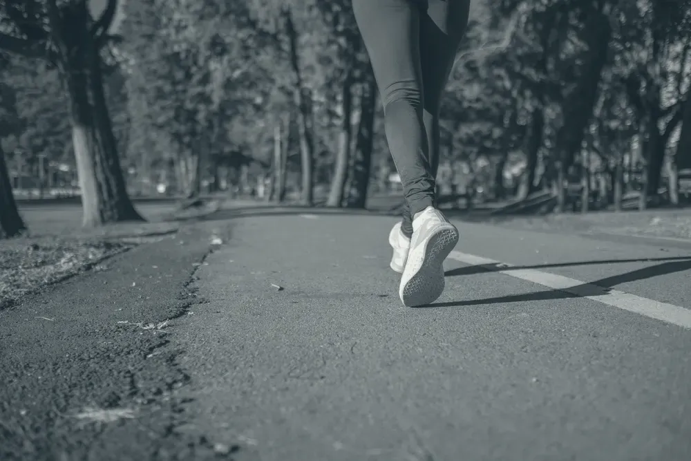 The legs of a person running along a tree-lined park path.