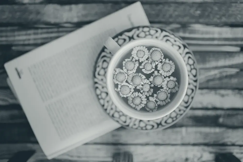 A cup of chamomile tea with dried flowers, seen from above on a wooden table.