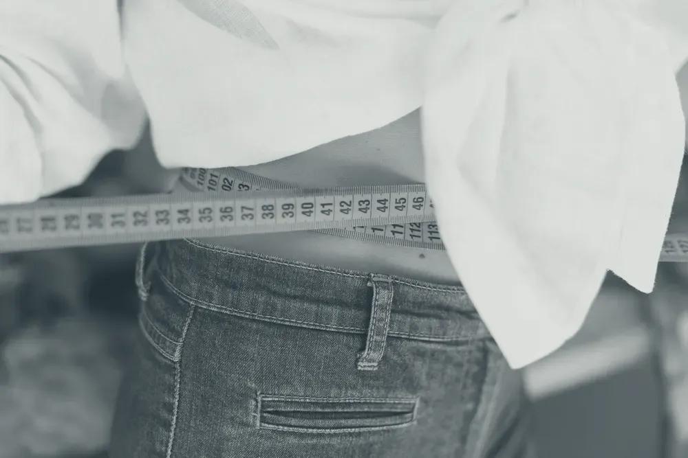 Hands measuring a waist with a tape measure, face out of frame.