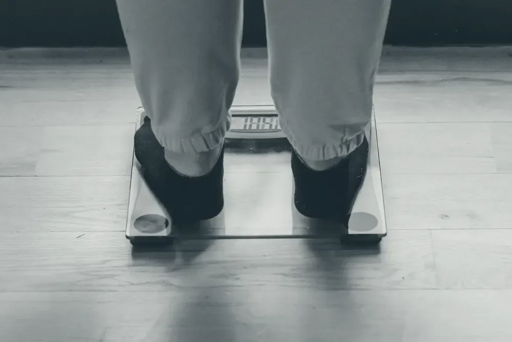 Feet in black socks on a digital glass scale, on a wooden floor.