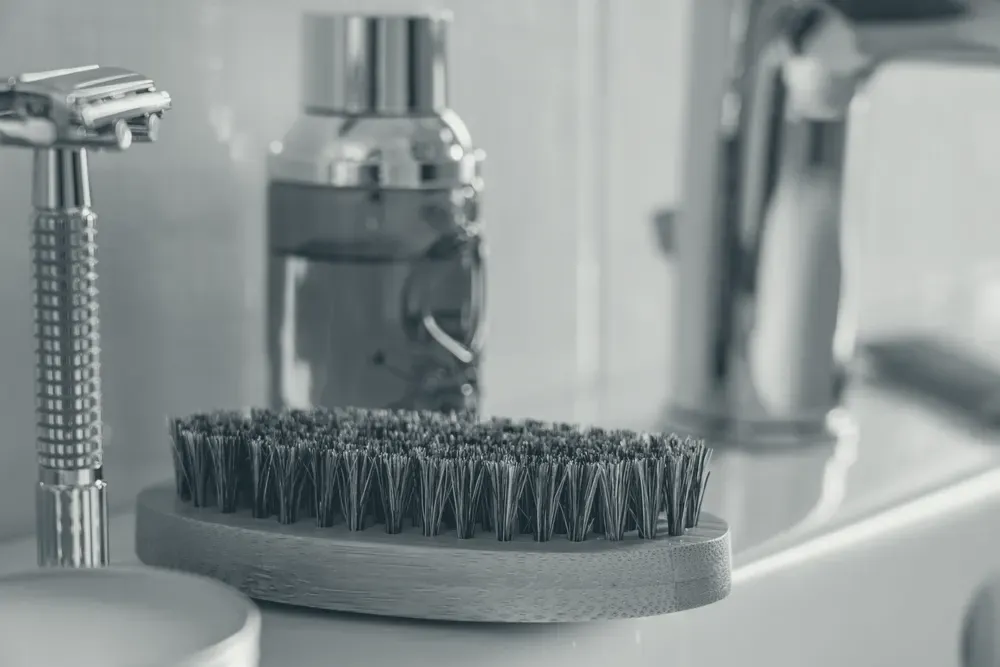 A wooden-bristle brush resting on a bathroom sink in natural light.