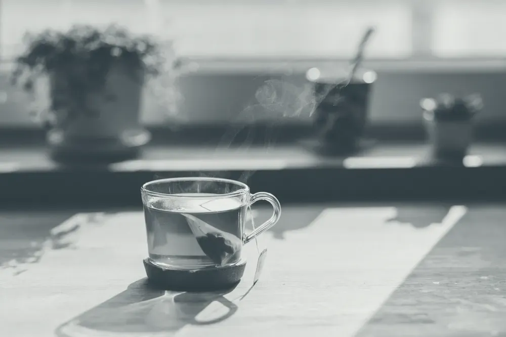 A glass cup of hot tea with steam rising, on a sunlit wooden table.