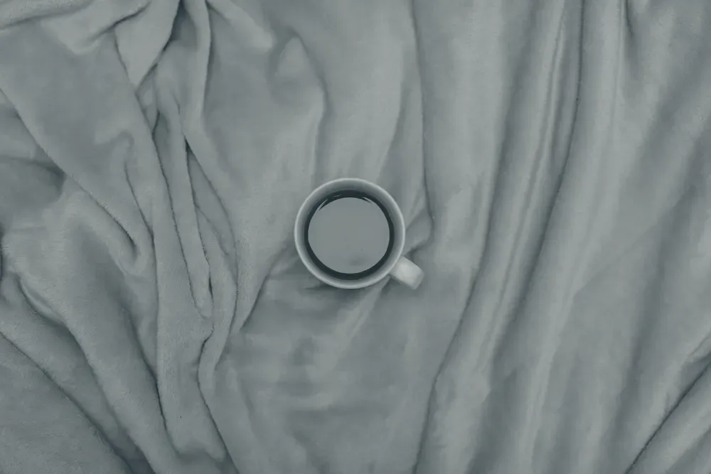 A cup of tea seen from above, resting on a soft folded blanket.